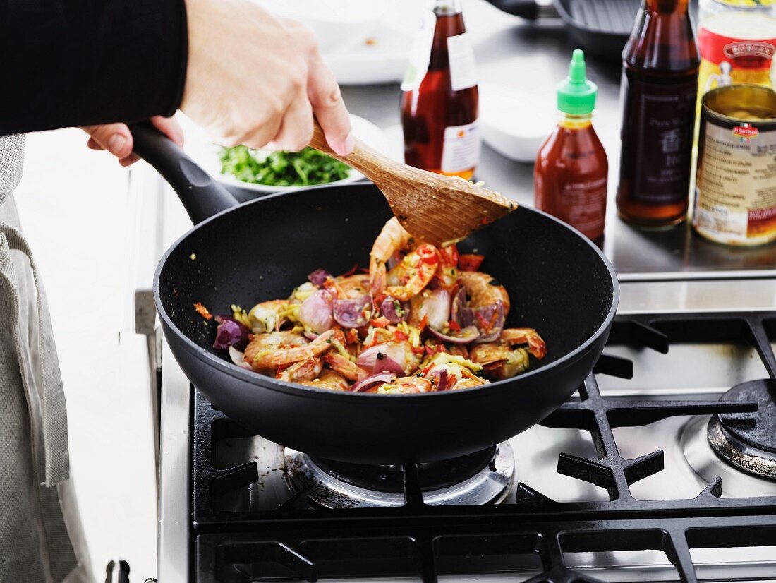 A person frying prawns with onions and chilli in a pan