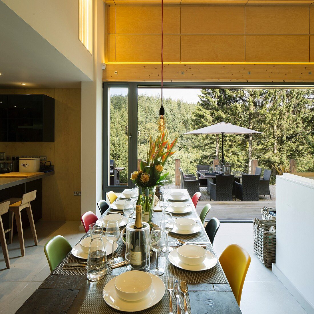 Set table and colourful chairs in open-plan interior; view of furnished terrace in background