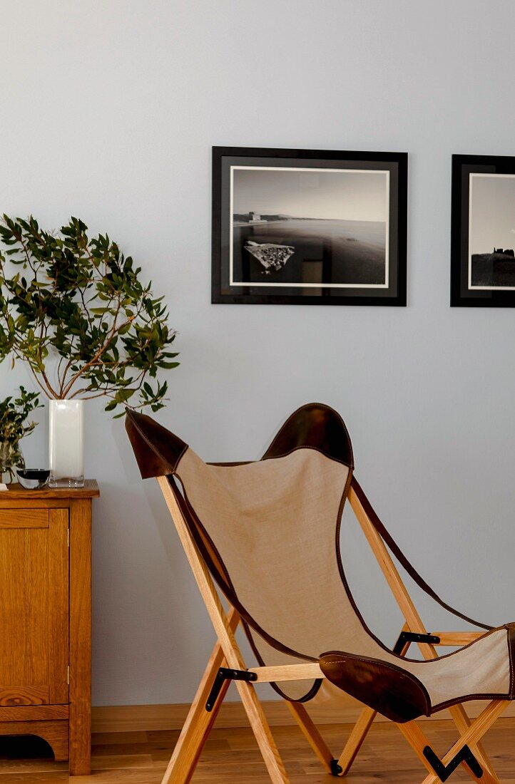 Classic canvas chair with wooden frame in front of framed photos on wall painted pale blue