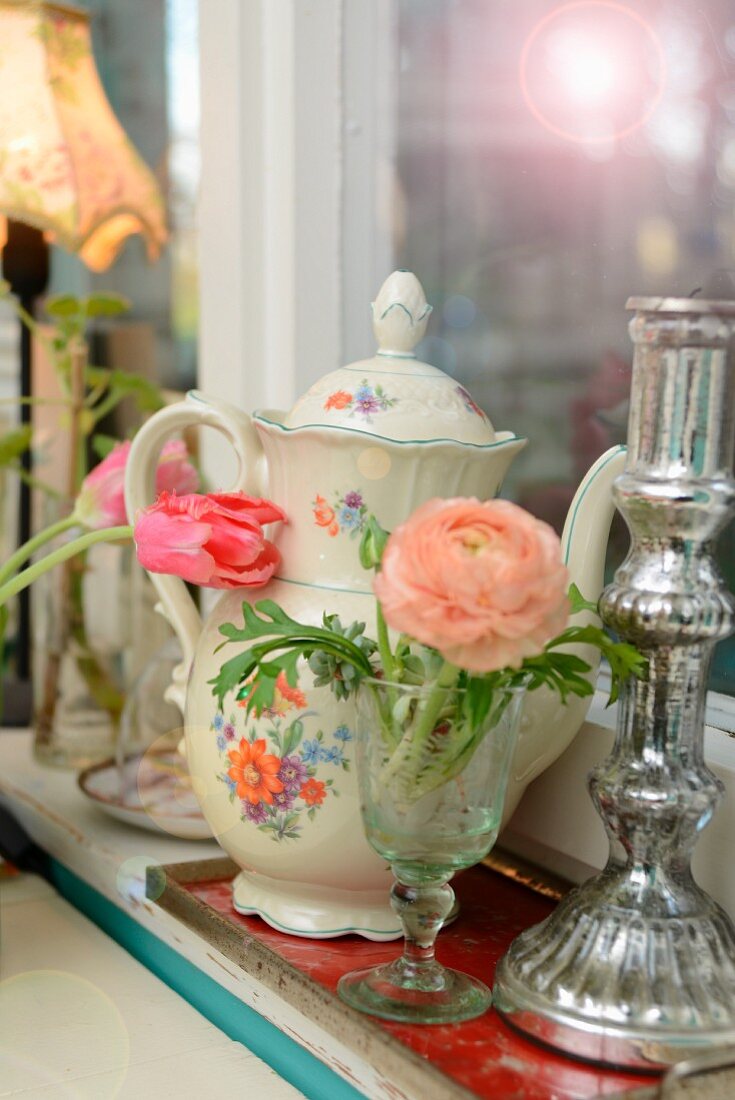 Salmon-pink ranunculus, candlestick and vintage-style coffee pot on windowsill