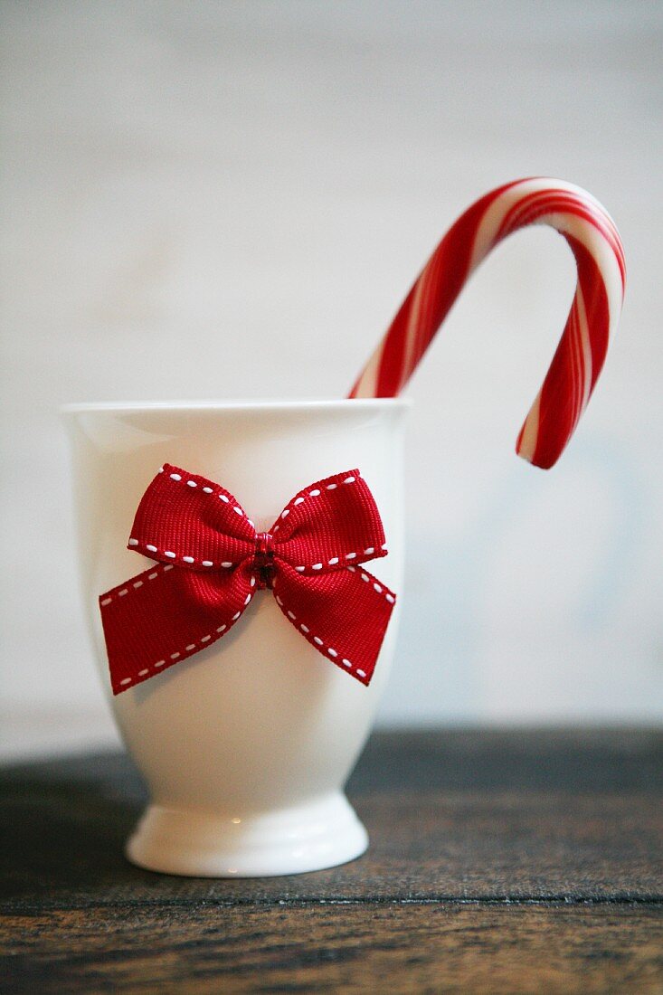 A candy cane in a white porcelain egg cup with a red bow