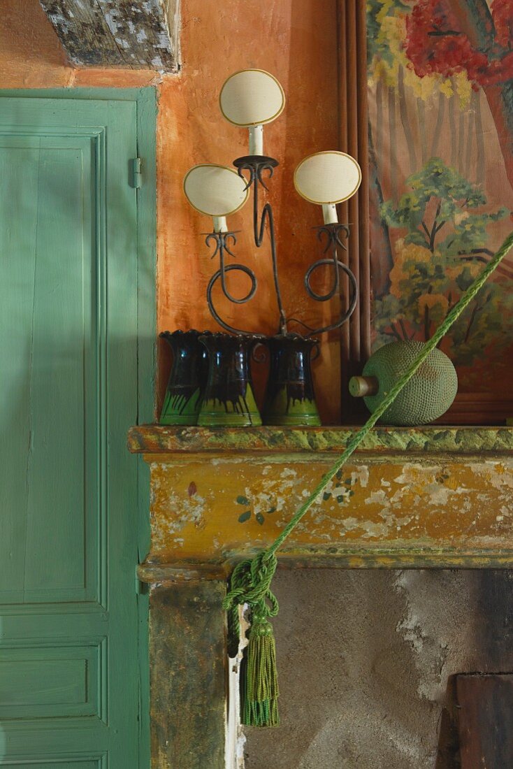 Collection of vases and vintage-style table lamp on mantelpiece with peeling paint