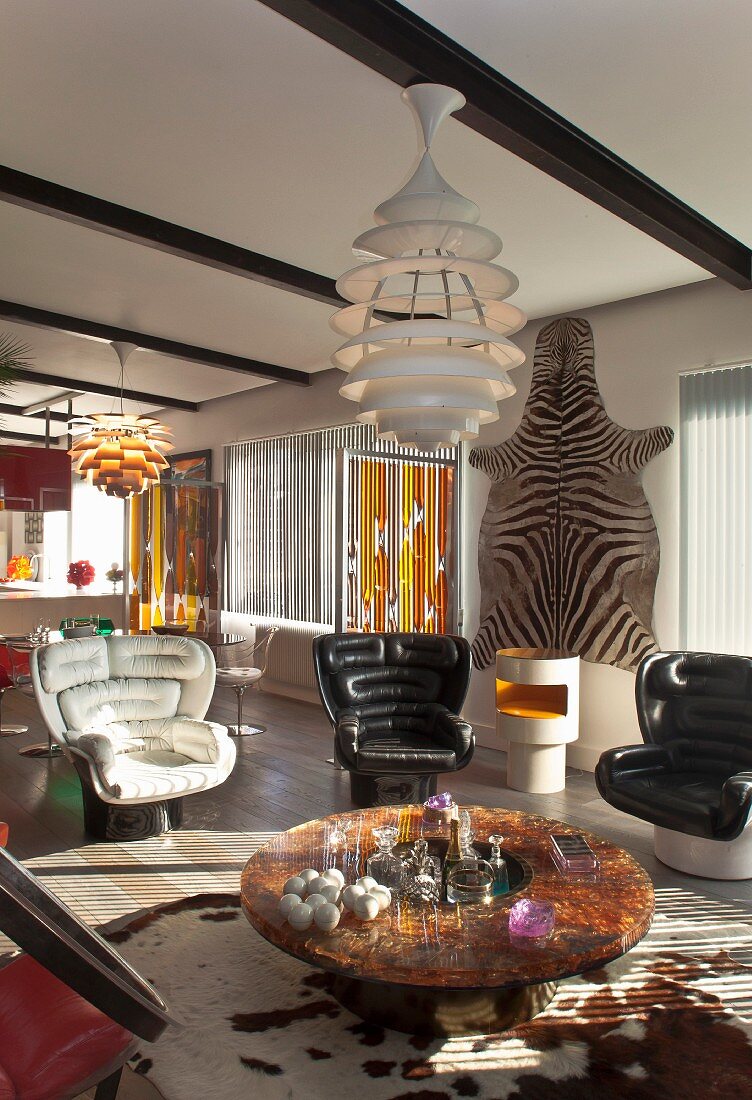 Retro black and white leather armchairs around round coffee table and designer lamp in front of zebra skin on wall