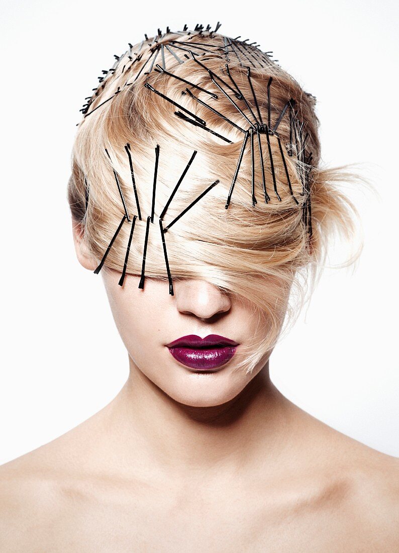 A blonde woman wearing lots of hair pins with her hair over her eyes