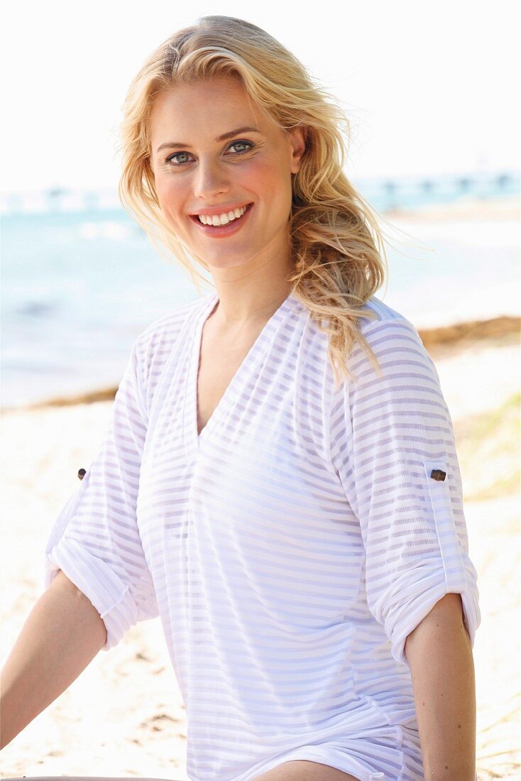 A young blonde woman on a beach wearing a transparent striped top