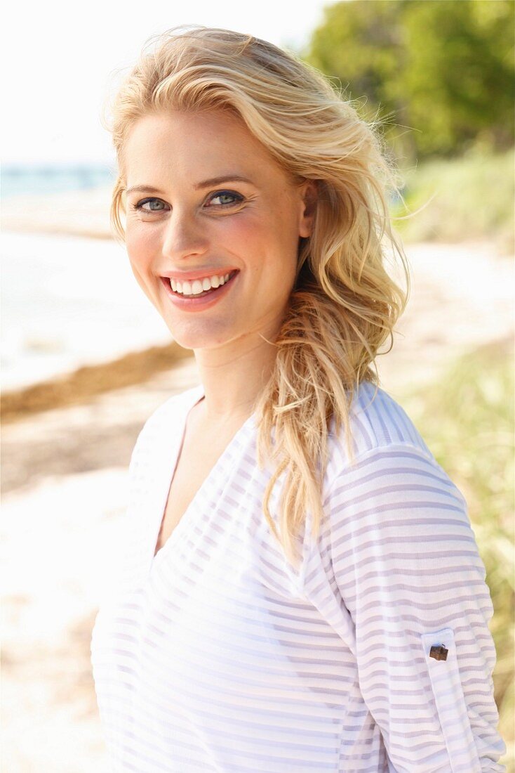 A young blonde woman on a beach wearing a transparent striped top