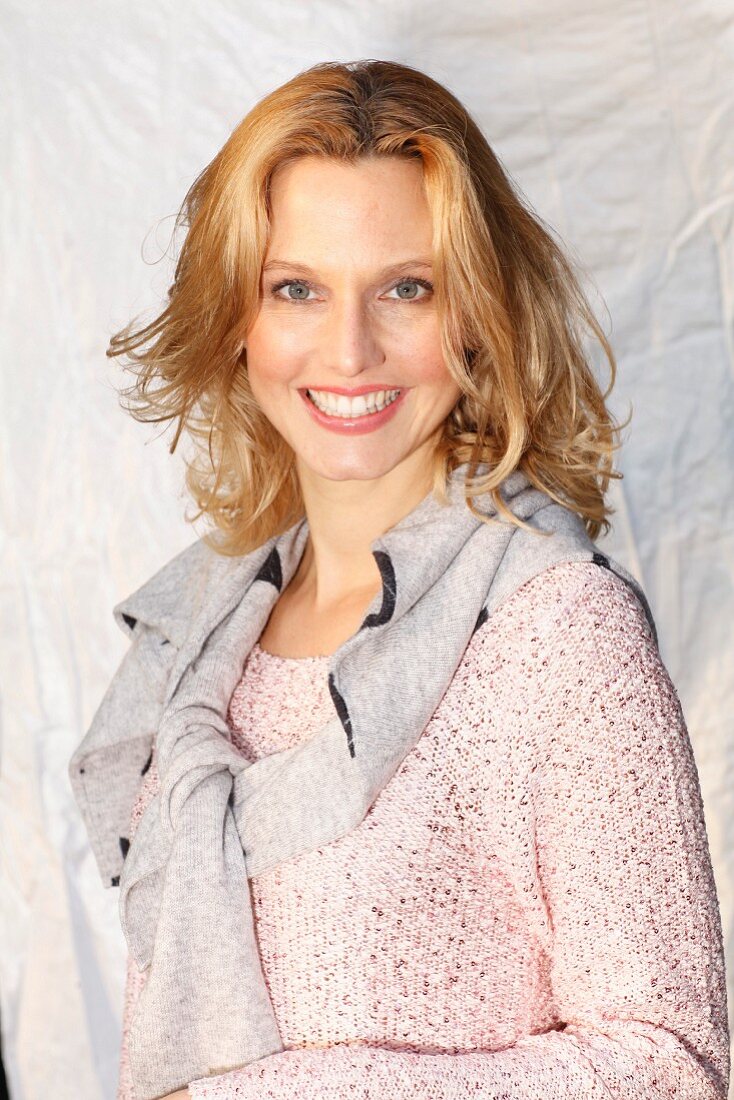 A blonde woman wearing a pastel pink jumper with Lurex and sequins