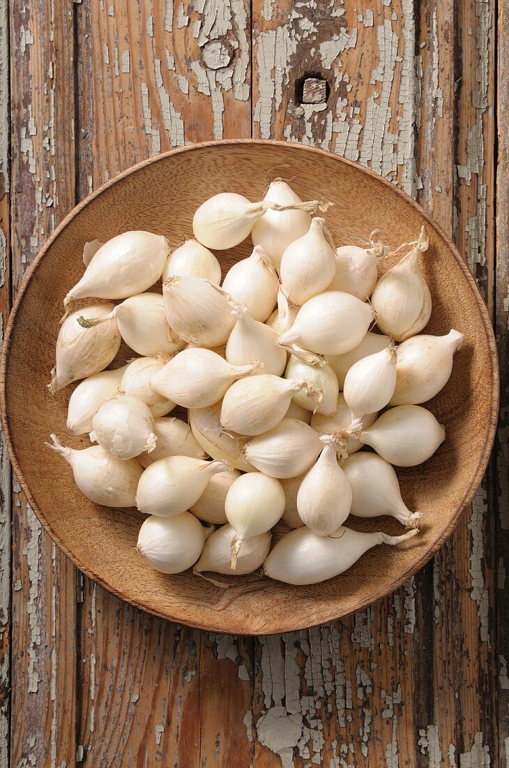 Small white onions on a wooden plate (seen from above)