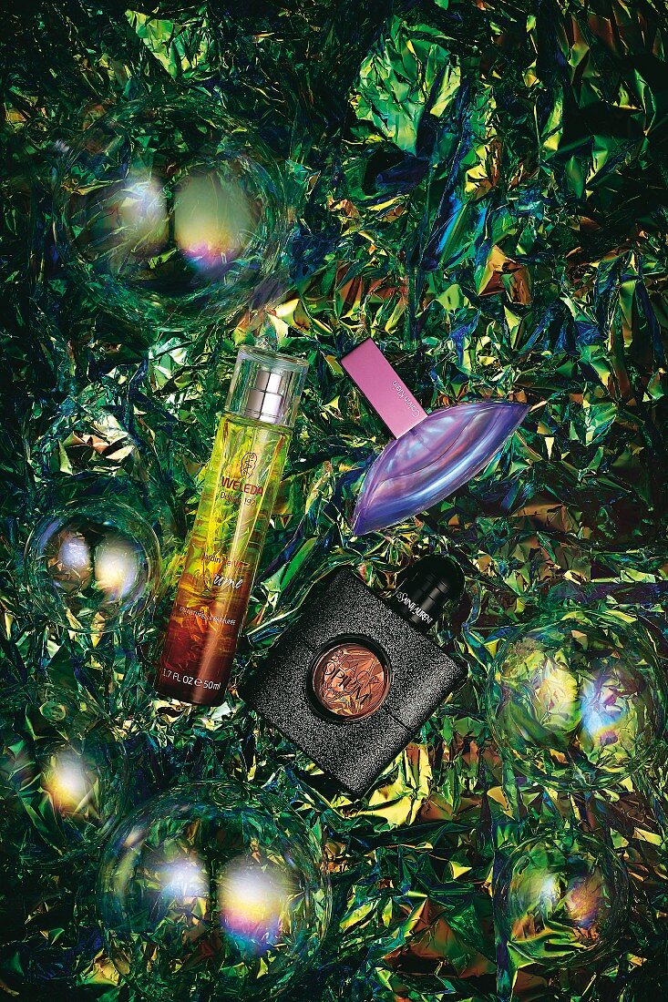 Three bottles on branded perfume on shiny green foil with soap bubbles