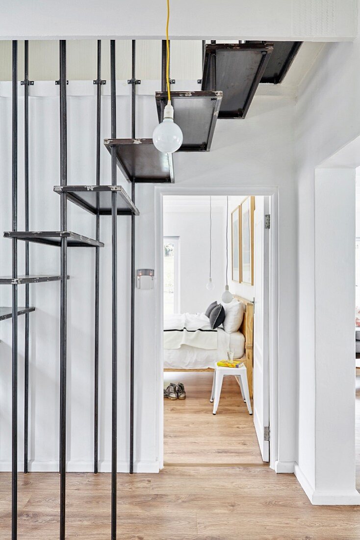 Steel staircase in hallway and view of retro stool next to bed seen through open door