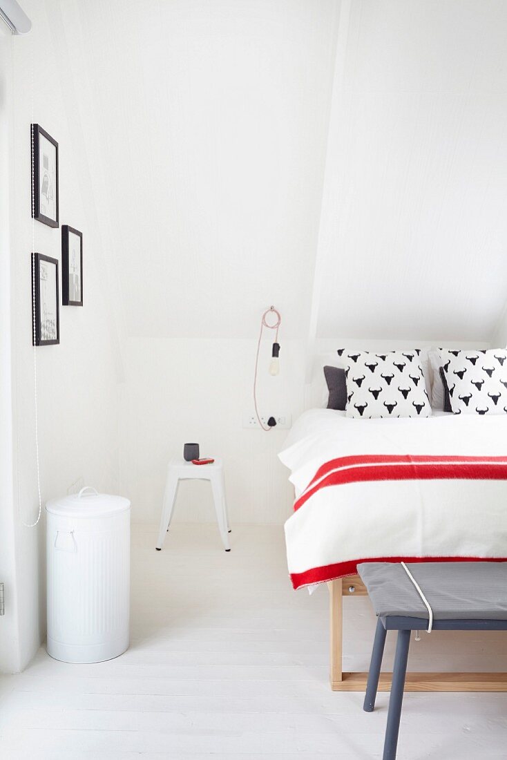 Bed with red-and-white-striped bedspread and retro stool used as bedside table in attic bedroom