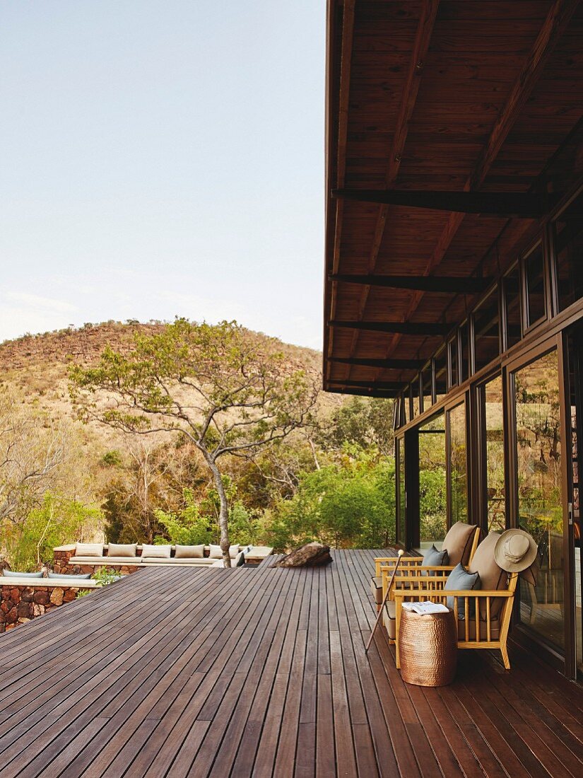 Armchairs against glass wall on wooden terrace with uninterrupted view of wild landscape