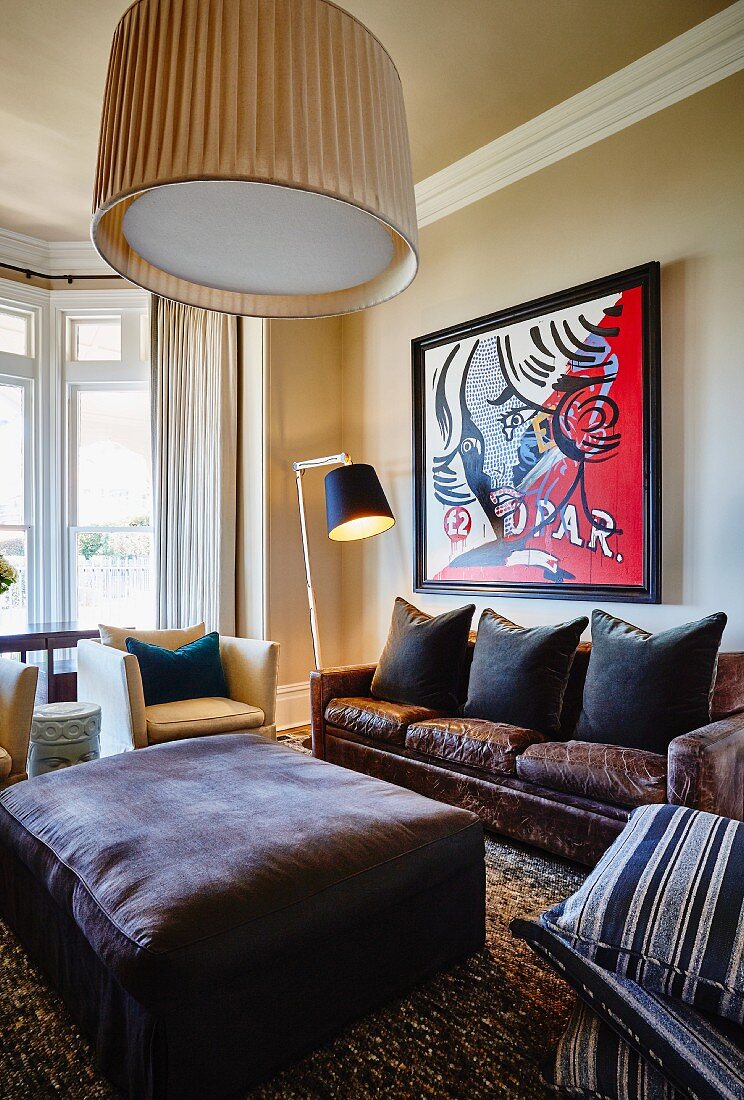 Ottoman, cushions arranged on leather sofa below modern artwork on wall