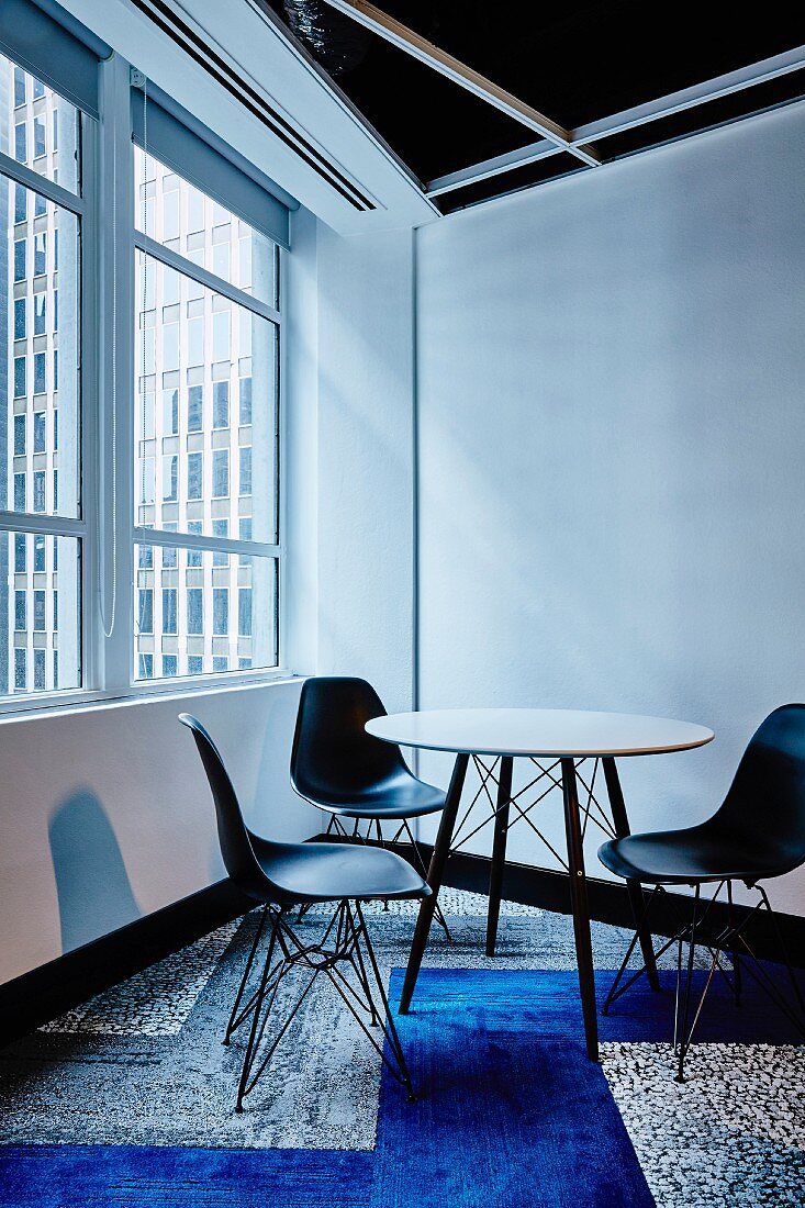 Round table and black classic shell chairs in corner on patchwork carpet