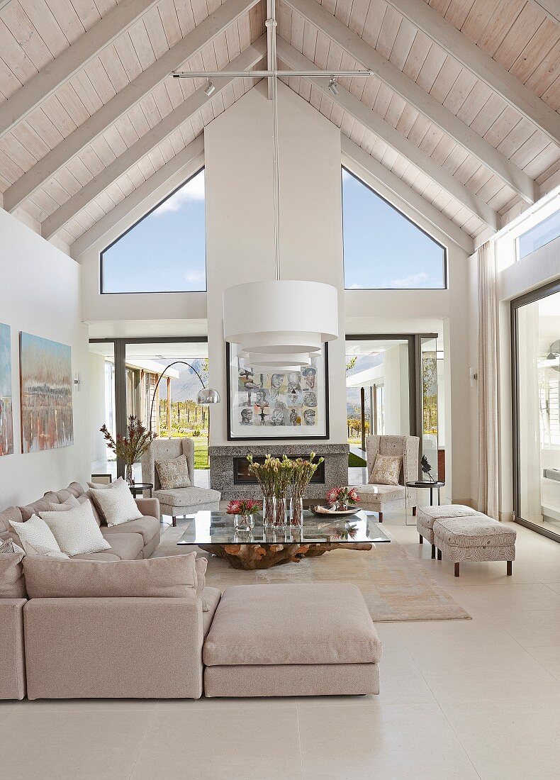 Open-plan, elegant interior with exposed roof structure painted white, pale grey corner couch and glass table
