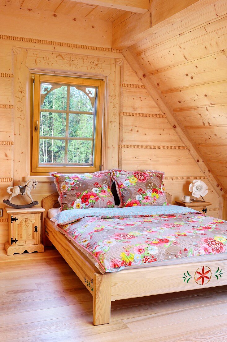 Double bed with floral bed linen in attic room with pale wooden cladding