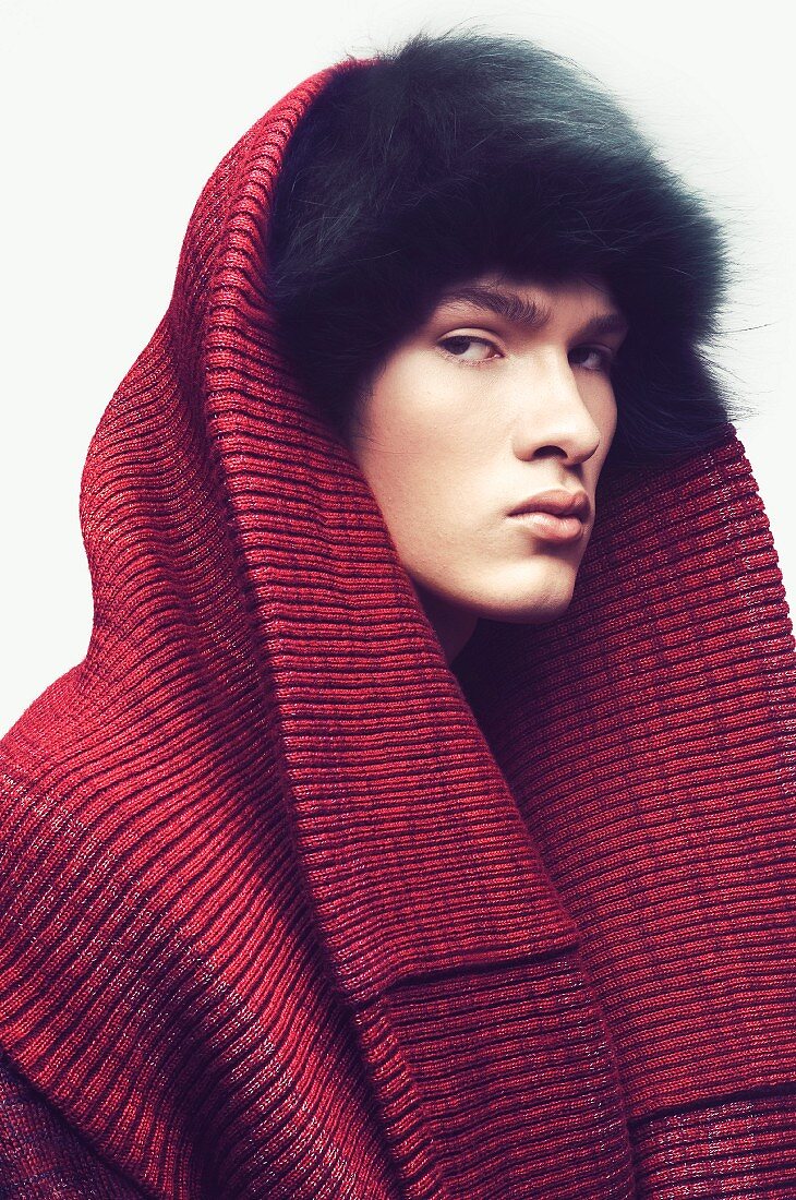 A young man wearing a black fur hat, wrapped in knitted fabric