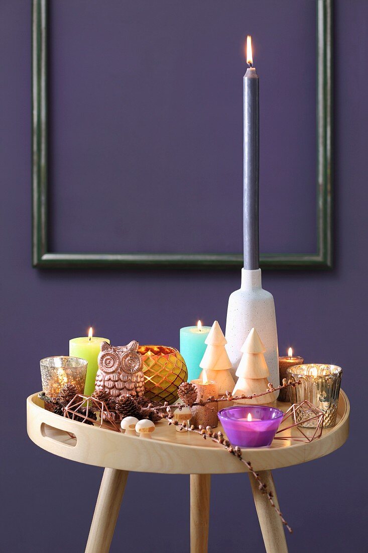 Colourful collection of candles on tray table in front of purple wall