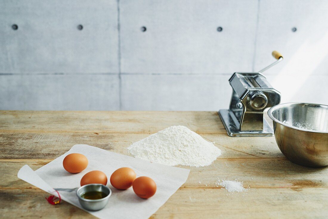 Ingredients for pasta dough and a pasta machine on a wooden table