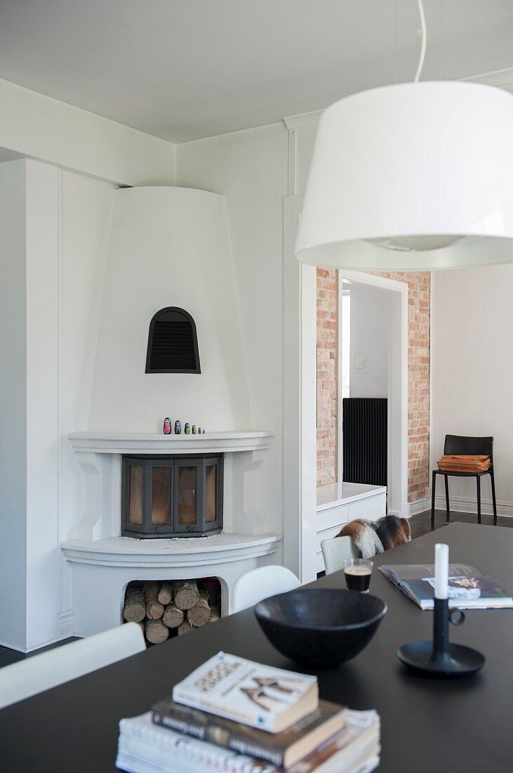 White pendant lamp above black table in front of corner fireplace with firewood niche