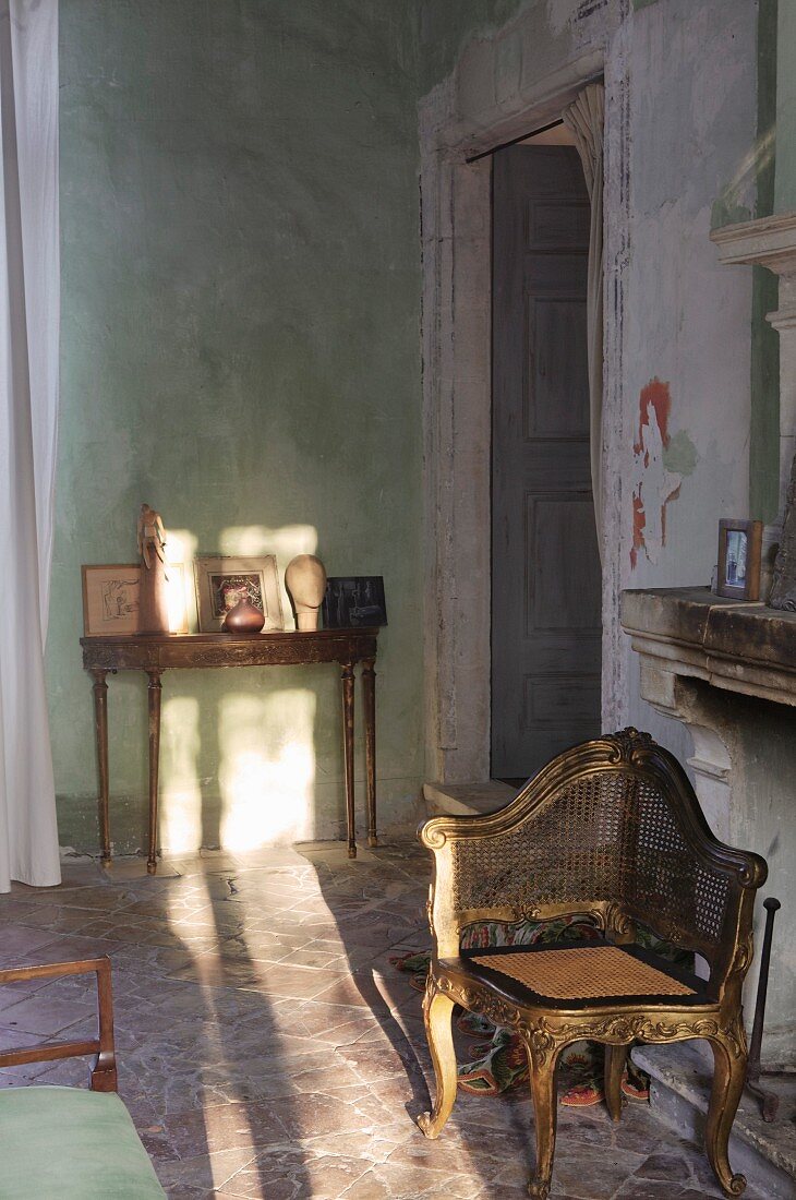 Antique chair with gilt Rococo-style wooden frame and delicate washstand in rustic Mediterranean interior