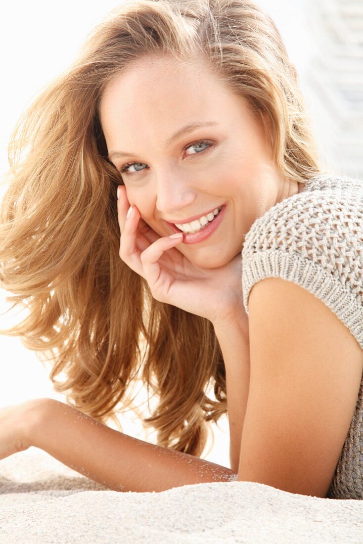 A young blonde woman lying on the beach wearing a knitted top