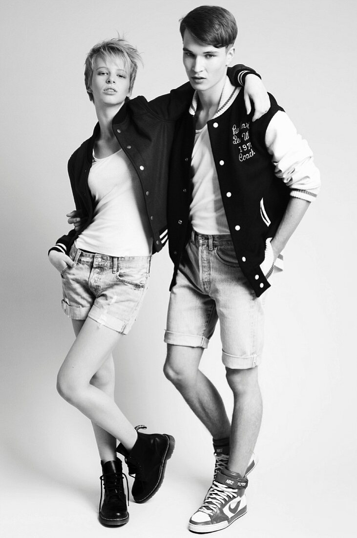 A young couple wearing cropped jeans and varsity jackets (black-and-white shot)