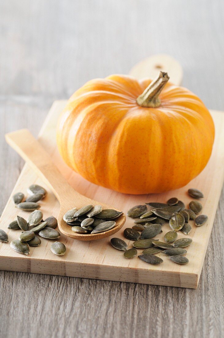 A mini pumpkin and pumpkin seeds on a chopping board