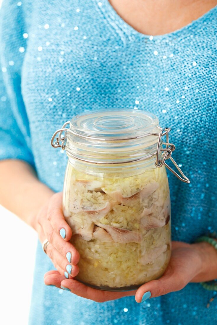 A woman holding a jar of herring with onion and vegetable oil