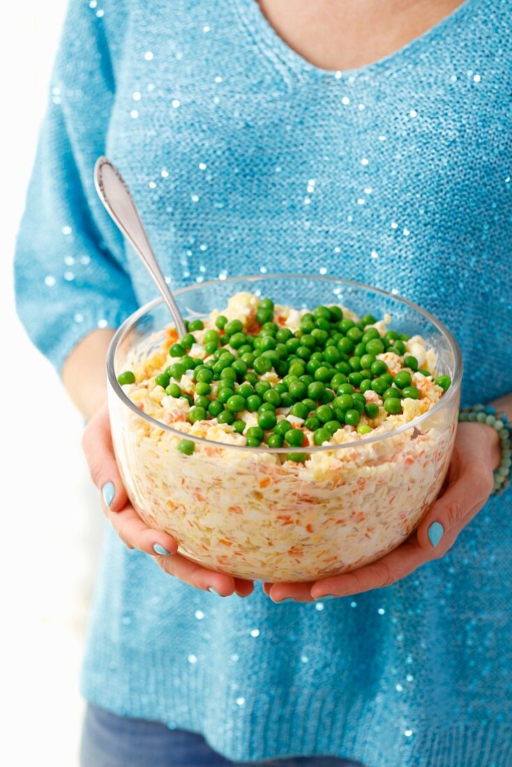A woman holding a glass bowl of vegetable salad with mayonnaise