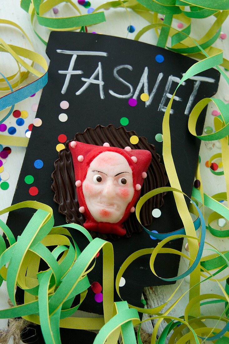 A marzipan carnival mask on a slate with paper streamers