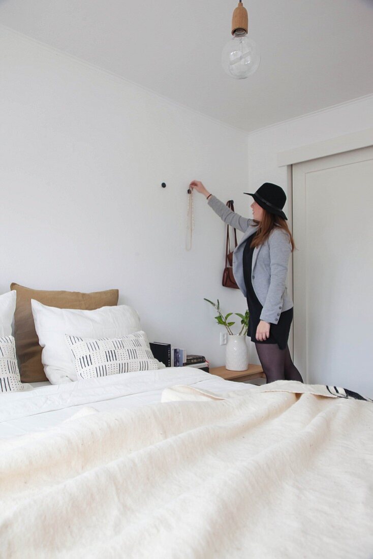 Woman hanging necklace on wall hook in bedroom