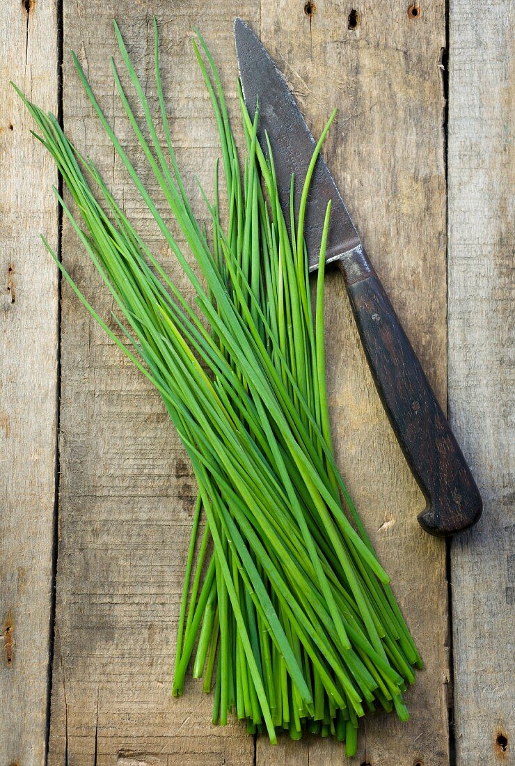 Fresh chives with a knife on a wooden surface