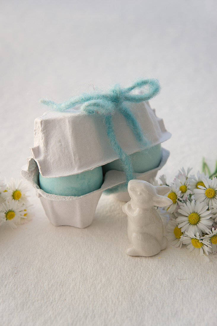 Pale blue Easter eggs in egg box, Easter bunny and daisies