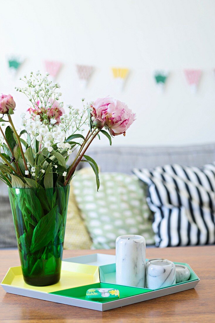 Pink peonies in green glass vase and tealight holder on tray