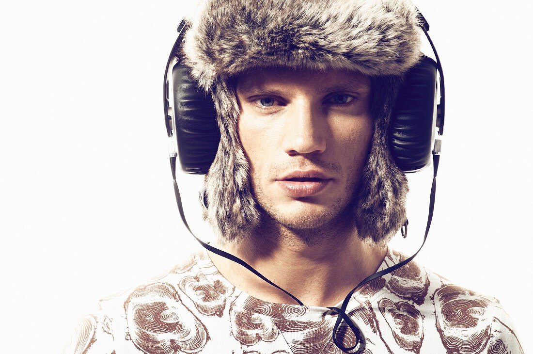 A young man wearing a patterned shirt, a fur hat and headphones