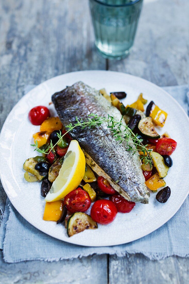 Trout on a bed of grilled vegetables with a lemon wedge