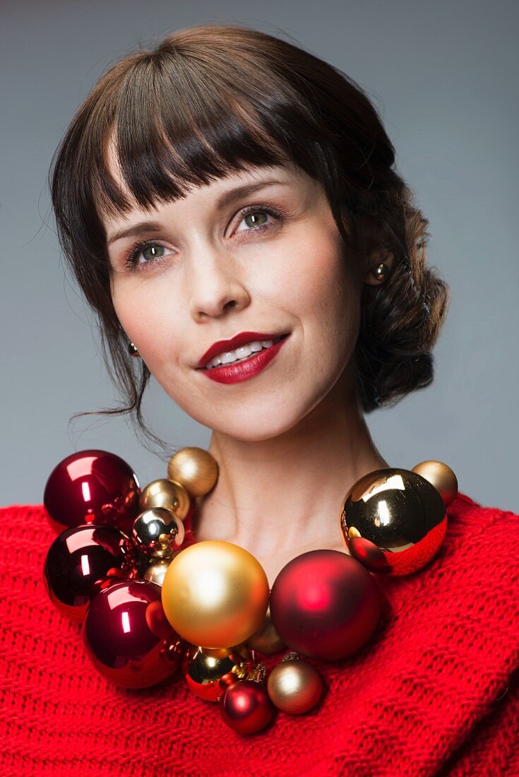 Dark-haired woman wearing red dress and necklace of Christmas-tree baubles