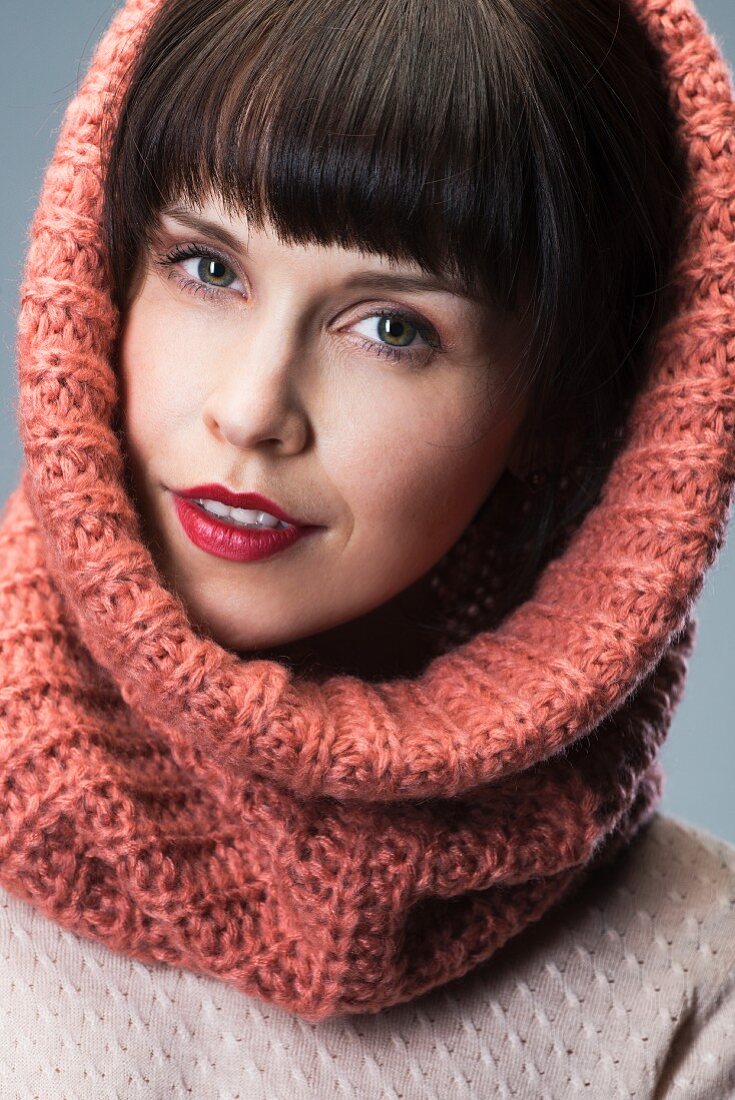 Dark-haired woman wearing salmon pink loop scarf