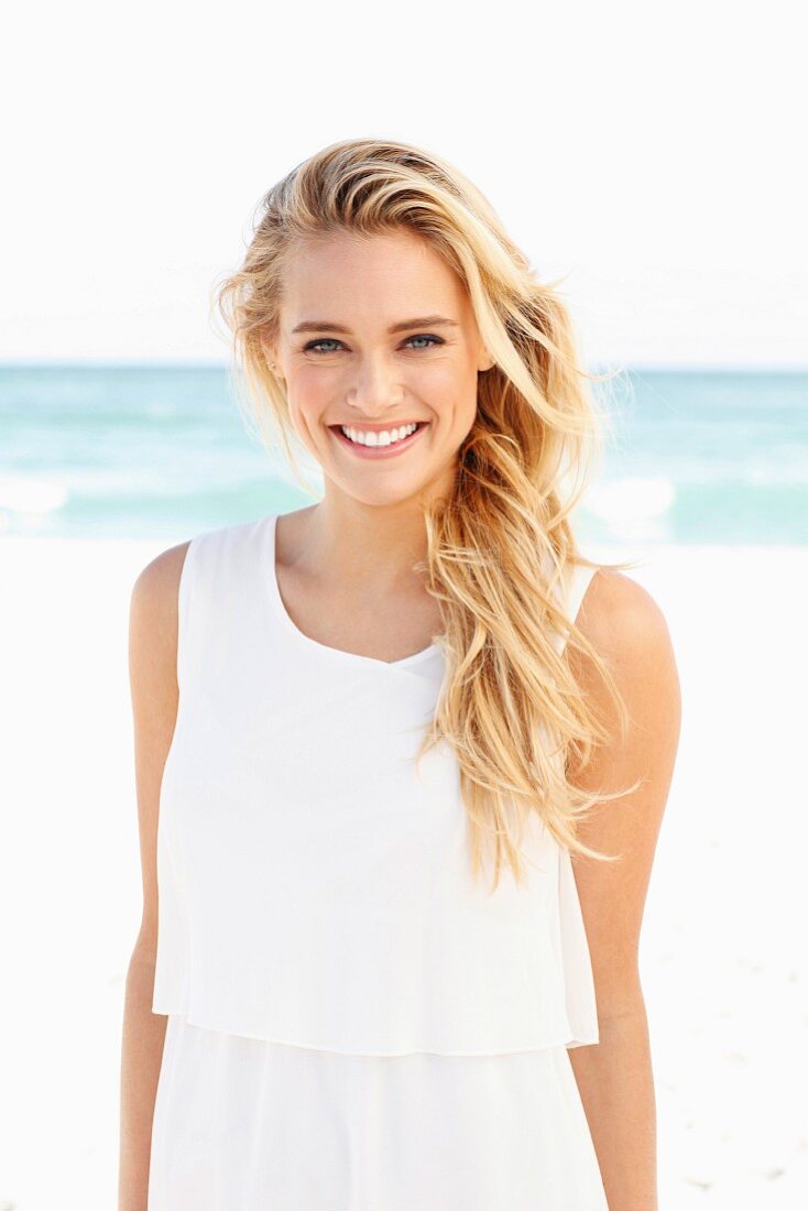 Young blonde woman wearing white dress on beach