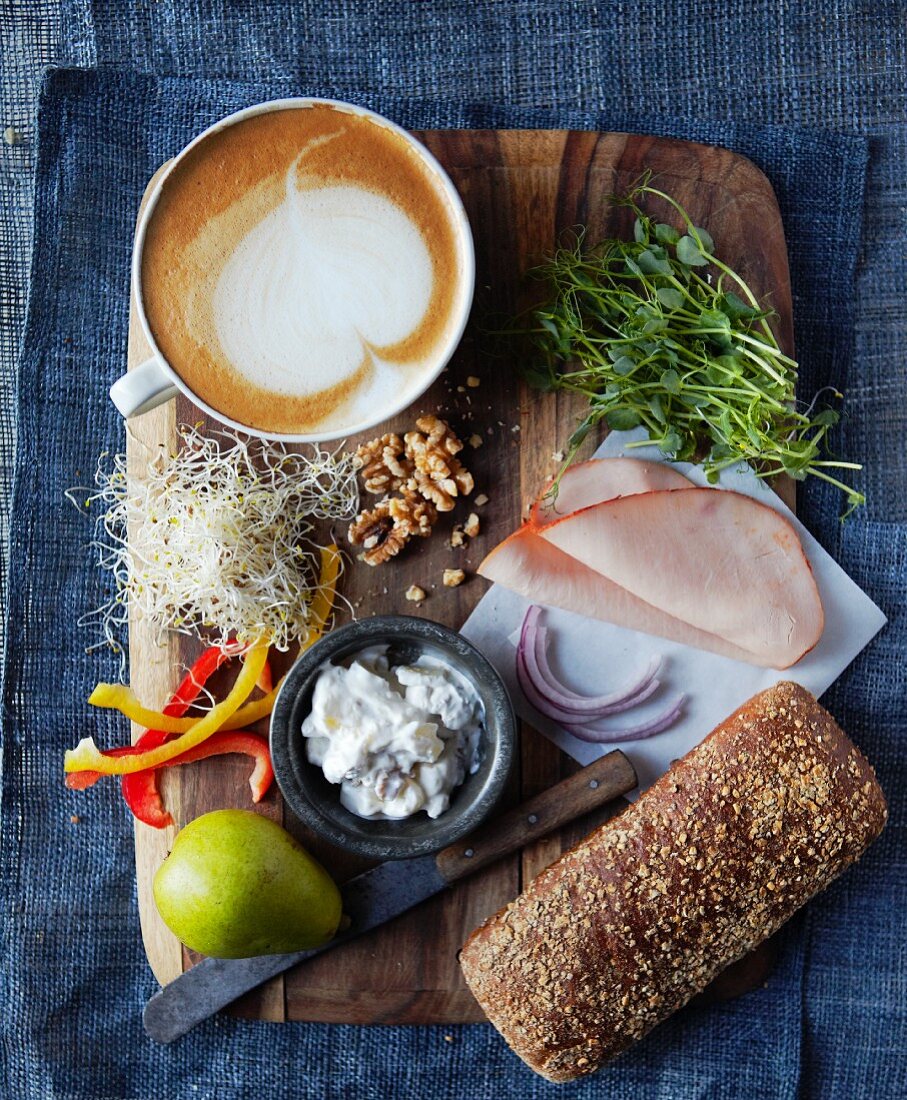 Ingredients for a turkey sandwich (turkey ham, pears, cottage cheese, pepper, walnuts, alfalfa sprouts and red onions) with a cafe latte