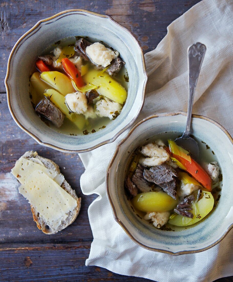 Beef soup with dumplings and vegetables served with a slice of bread and cheese
