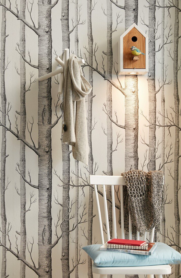 A bird house with a built in spotlight hung on a wall with tree-patterned wallpaper