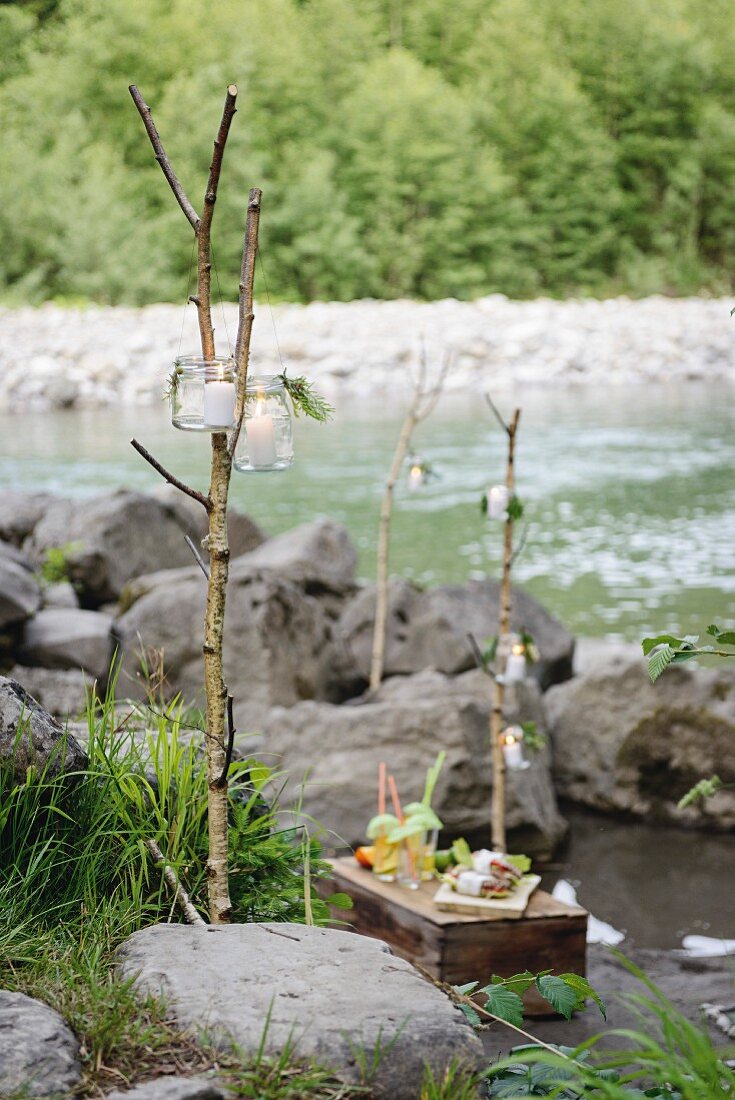 Picnic on wooden crate on river bank with candle lanterns hung from branches