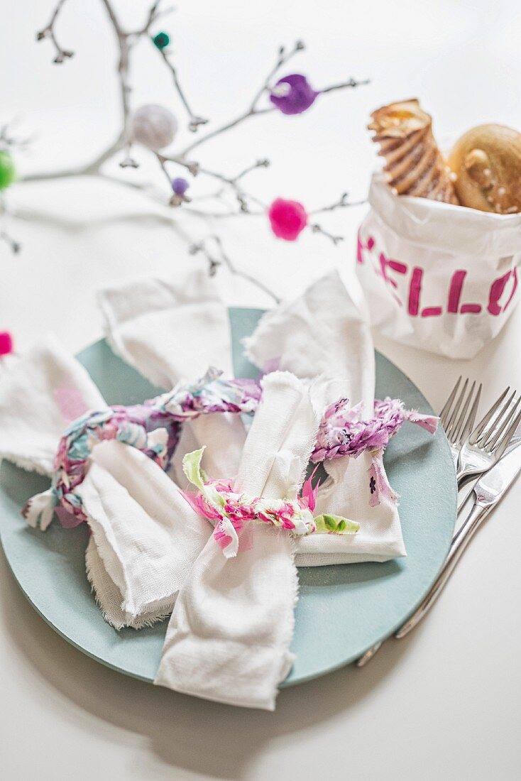 Fabric remnants used as decorative ribbons for linen napkins in front of hand-made fabric bread bag decorated with motto 'HELLO'