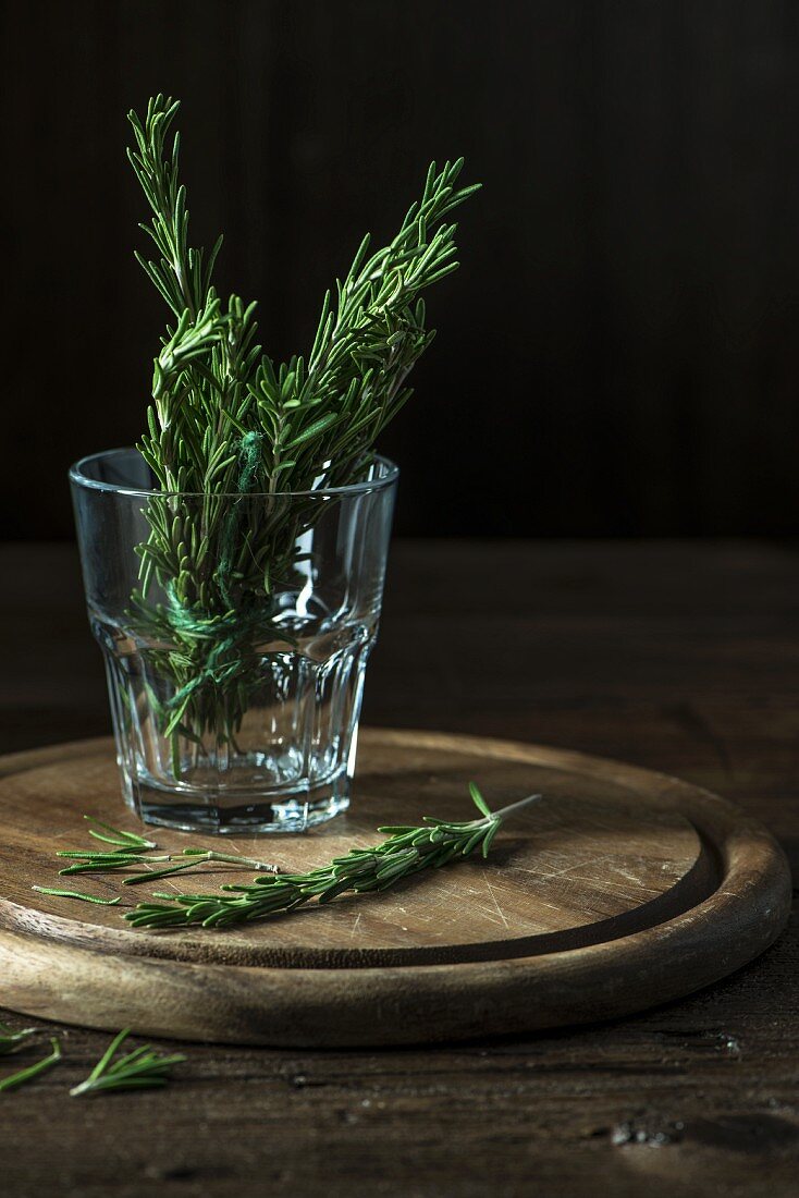 Rosemary sprigs in a glass of water on a round wooden board