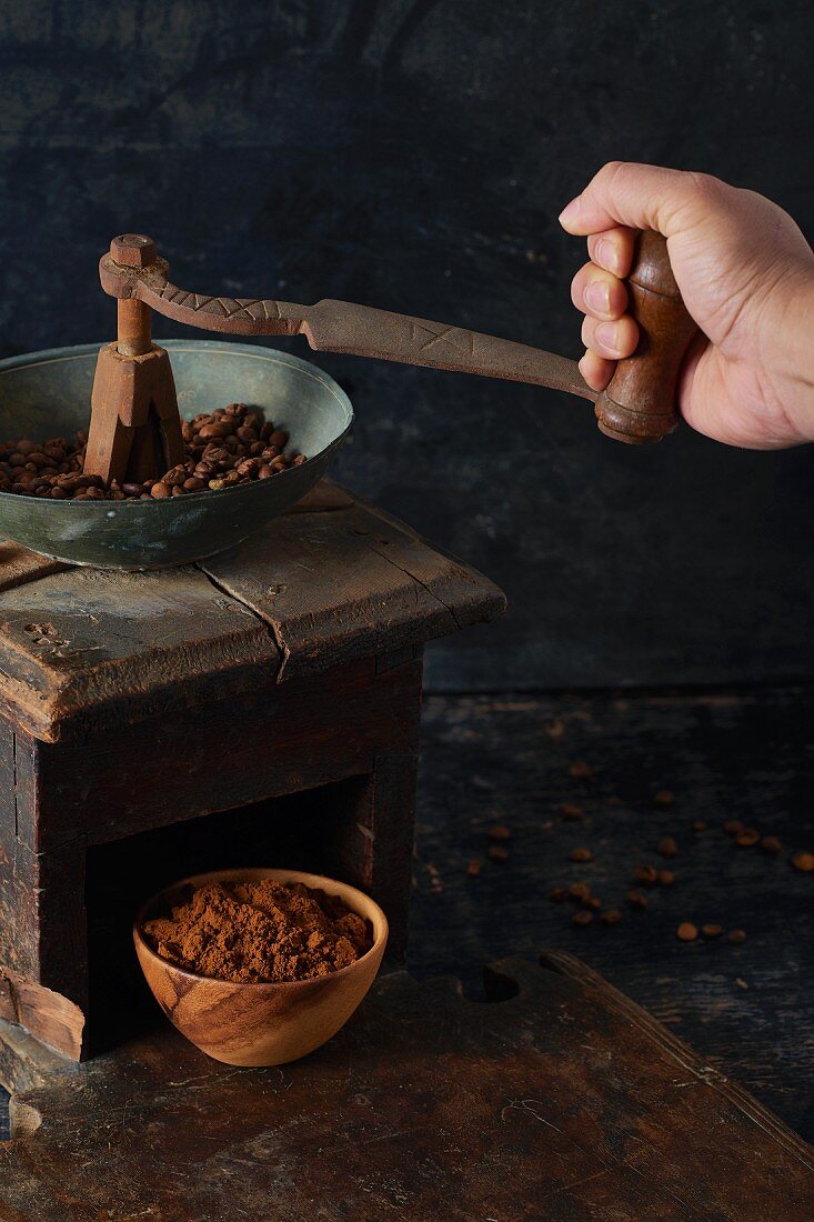 Coffee beans being ground in an antique wooden grinder