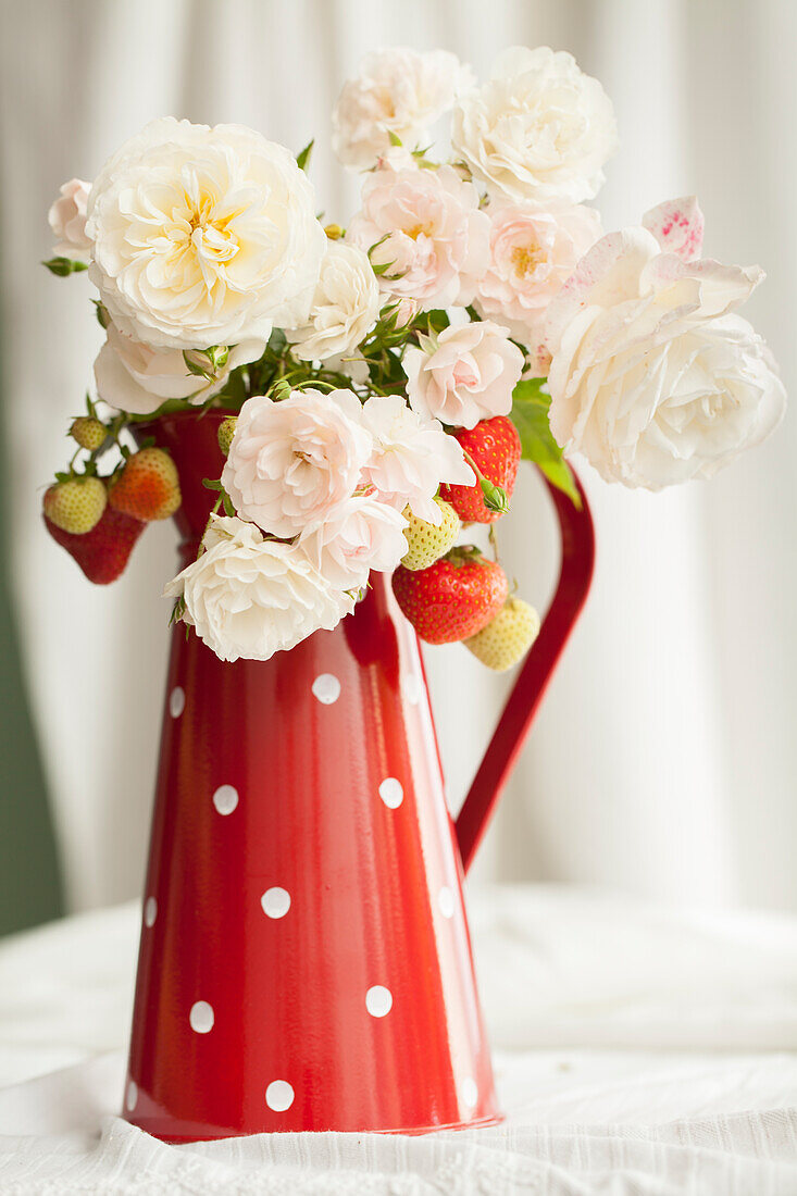 Summer bouquet of white garde roses & sprigs of strawberries in red enamel jug