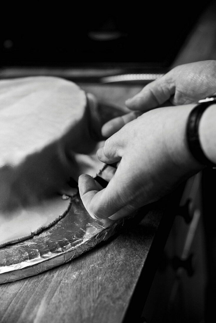 A wedding cake being covered with fondant icing (black-and-white shot)