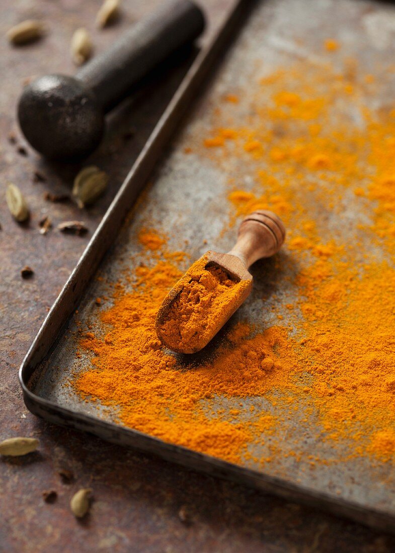 Turmeric powder with a wooden scoop on a baking tray